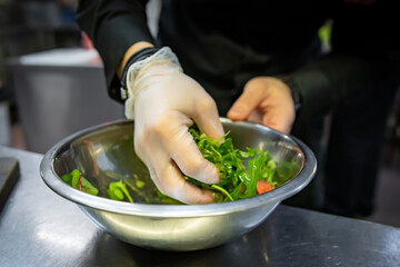Chef hand mixing a vegetable salad in stainless steel bowl on kitchen