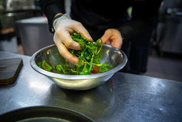 Chef hand mixing a vegetable salad in stainless steel bowl on kitchen