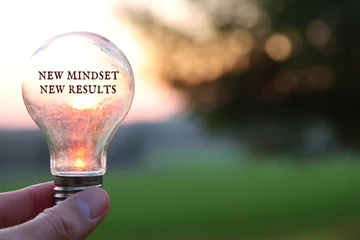 Foto op Plexiglas Hand holding light bulb with the text new mindset in front of the bright sun © tomertu