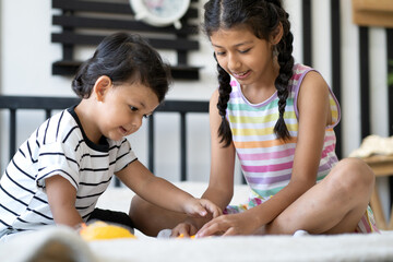 Fototapeta premium Sister and cute brother boy have fun sitting in bed together playing toy car at home. Portrait of adorable Asian girl love and care for her little kid preschool sibling. Two children bonding in family