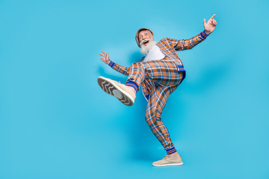 Full length photo of cool excited retired man dressed plaid suit walking rising leg empty space isolated blue color background
