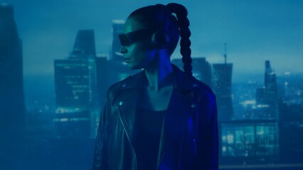 Portrait of cyberpunk girl with a smartphone in a glasses and headphones. Beautiful young woman on...