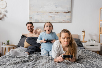 KYIV, UKRAINE - NOVEMBER 28, 2022: cheerful mother, father and excited child playing video game in bedroom