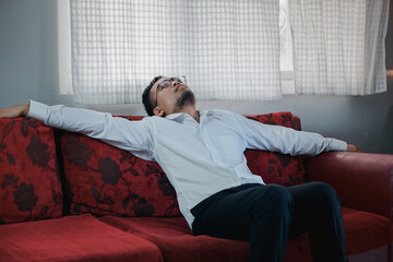 Obraz premium Asian young upset depressed man sitting alone in living room at home. Attractive unhappy male feeling very sad, lonely and frustrated with life problem think of money debt, bankruptcy. 