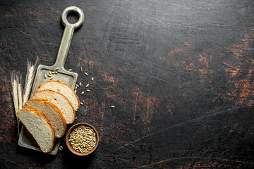 Pieces of bread on a cutting Board with grains and spikelets.