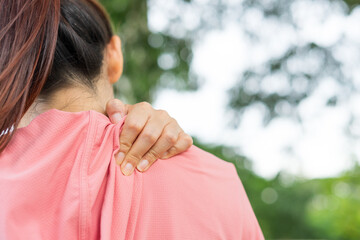 Young woman in sports outfits pink injured her shoulder during exercise in the park. Upper section of sports girl suffering from shoulder pain while sitting at workout. Accident from exercise concept.