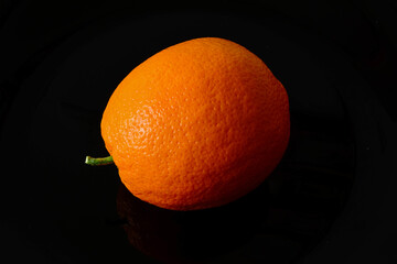 Isolated ripe orange fruit in close-up view. Black background. white and yellow orange peel. vitamin and healthy eating concept. vegetarian lifestyle. still life macro image.