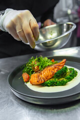 chef hand cooking salmon steak with broccoli and salad on restaurant kitchen