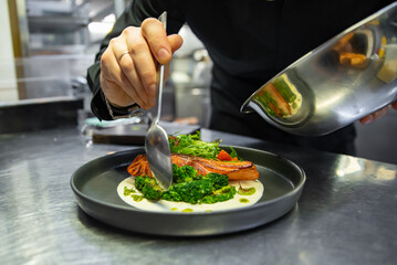 chef hand cooking salmon steak with broccoli and salad on restaurant kitchen