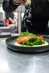 chef hand cooking salmon steak with broccoli and salad on restaurant kitchen