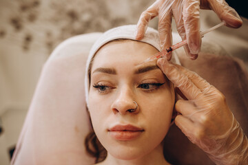 Naklejka premium Portrait of young Caucasian woman getting botox cosmetic injection in forehead. Beautiful woman gets botox injection in her face.