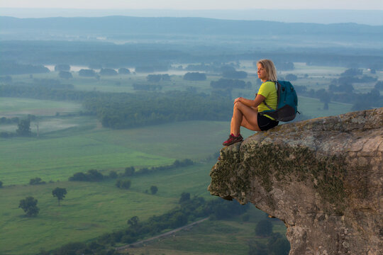 Woman sitting on sandstone overhang watching sunrise from summitÂ ofÂ PetitÂ Jean MountainÂ above Arkansas River ValleyÂ 