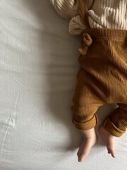 baby's small legs in brown pants with suspenders on a white fabric background