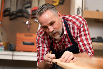Professional elder carpenter using sandpaper to clean wood after cutting, making wood smooth without splintering before assembly furniture. Senior joiner skill focuses a perfectionist of woodcraft.