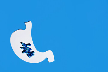 Anatomical silhouette of the stomach with natural blue pills inside. The concept of treating with excessive amounts of pills. Flat lay, space for text.