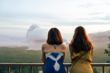 Mother and daughter traveler traveling together,  standing at view point to see the natural mountain in a sea with fog cover in the morning. Family love relationship, family concept.