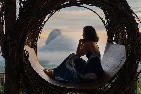 Mature woman sitting on a hanging chair, looking at the island view in the ocean during a holiday at a resort in the morning,  relaxation trip with family. 