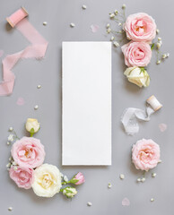 Fototapeta na wymiar Blank paper card between pink roses and pink silk ribbons on grey top view, wedding mockup