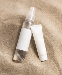 Cream bottles with blank label on beige sand close up. Cosmetic packaging mockup