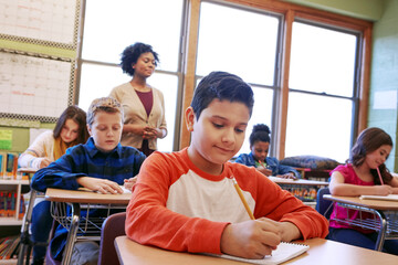 Children, education or kids in classroom writing in notebook for learning, research or study for exam with teacher. Scholarship, thinking or students happy in school for test, academy or assessment