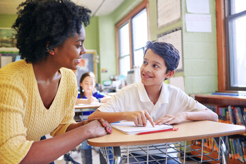 Learning, education and teacher help student with assignment in elementary school. Classroom support, scholarship and happy black woman or educator aid, explaining or helping male learner in class.