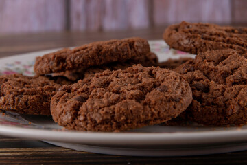 Tasty chocolate chip cookies on white plate on wooden background. Selective focus.