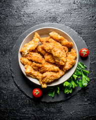 Chicken strips in a bowl with parsley and tomatoes.