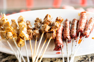 Close-up of grilled skewers of meat and chicken and sausages on a plate.