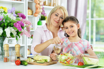 Cute little girl with her mother cooking together at kitchen table