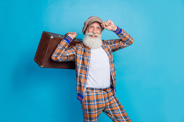 Photo of cheerful positive man pensioner wear checkered costume arm headwear rising baggage isolated blue color background