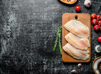 Fish fillet on a wooden cutting Board with rosemary and tomatoes.