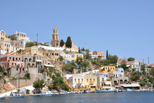 waterfront with boats and painted buildings of greek island Symi with blue sky on background