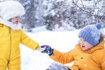 children playing in snow. little girl in yellow jumpsuit giving helping hand to boy sitting in the...