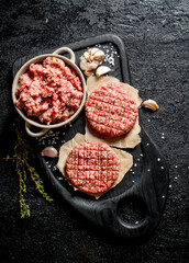Raw burgers and ground beef on a cutting Board with garlic and thyme.