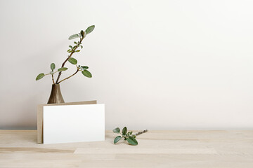 Mock-up of a blank invitation or greeting card in white and natural leaning on a brown vase with...