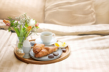 Fototapeta na wymiar Romantic breakfast in bed with flowers, croissant, coffee cup and hearts from chocolate on beige bed linen for valentines or mothers day, copy space, selected soft focus