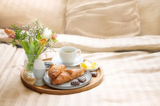 Romantic breakfast in bed with flowers, croissant, coffee cup and hearts from chocolate on beige bed linen for valentines  or mothers day, copy space, selected soft focus