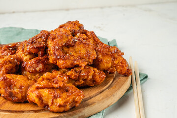Pieces of chicken in batter in a spicy Asian sauce close-up lie on a wooden board next to chopsticks, light background.