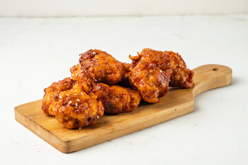 Fried chicken fillet in breadcrumbs and spicy Korean sauce lies on a wooden board for serving.