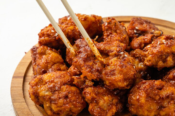 Spicy deep-fried chicken fillet in breaded, Korean style, close-up, chopsticks take a piece of chicken.