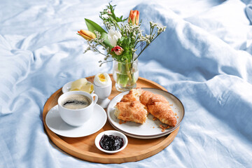 Happy morning with breakfast in bed, flowers, croissant, coffee and more on a tray on blue white...