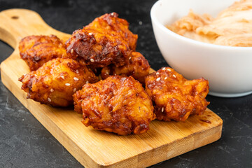 Pieces of fried chicken in Asian sauce on a wooden board close-up and kimchi. Korean chicken.