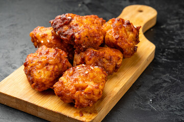 Pieces of spicy breaded chicken in red sauce in Korean close-up, a dish served on a wooden board, close-up.