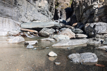 Puddle with crystal clear water and small pebbles and sands on the bottom, formed by Lillaz waterfall (Cascate di Lillaz) in granite crack, close bright view, Aosta valley, Italy