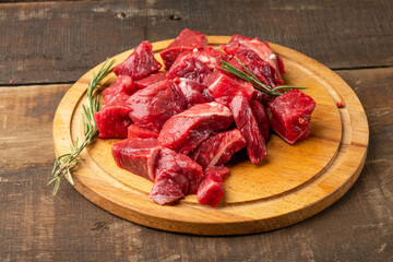 Beef meat diced raw with rosemary on a round shaped cutting board and wooden background.