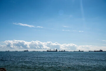 Coastal view of a freighter over the sea under clear skies and clouds. A number of trading ships are floating gently on the sea. High resolution photo editing image source