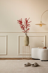 Interior design of living room interior with copy space, vase with rowan, white pouf, beige rug, round coffee table, stylish lamp, wall with stucco and personal accessories. Home decor. Template.