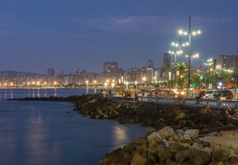 City of Santos, Brazil. Edge of the beach. People sitting on the short wall enjoying the beginning of a summer night.