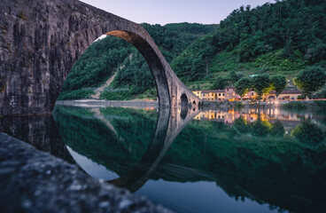 Il ponte del Diavolo o ponte della Maddalena a Borgo a Mozzano, in Toscana. Magica l'atmosfera con lo specchio d'acqua al crepuscolo. - obrazy, fototapety, plakaty