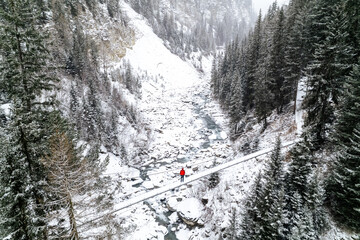 Aerial view of a person standing on a hanging bridge above a small river stream during winter...